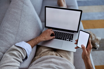 Above view of man using laptop while texting on mobile phone at home.