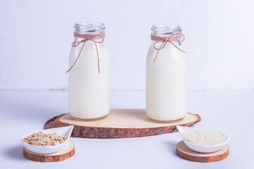 Rice and oat vegan milk in glass bottles on a wooden stand on a white background