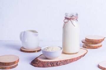Vegan rice milk in a glass bottle and rice in a white plate on a wooden stand on a white background
