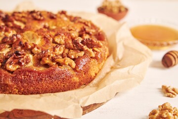 Closeup shot of a delicious apple walnut cake with honey surrounded by ingredients on a white table