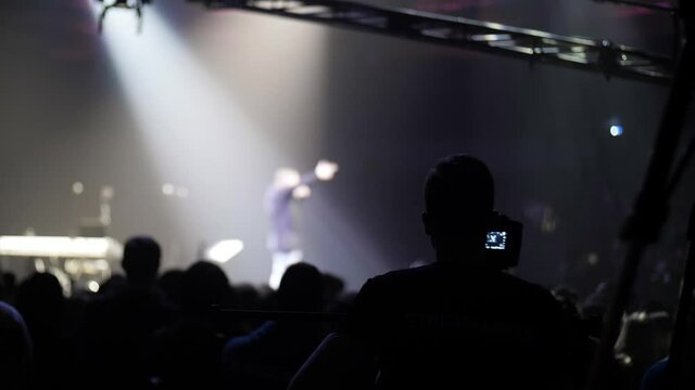 Video operator crane is shooting a crowd of people around the stage. Camcorder for shooting rock music concerts. Long boom crane. Self-isolation mode is over. Music band is playing on stage.