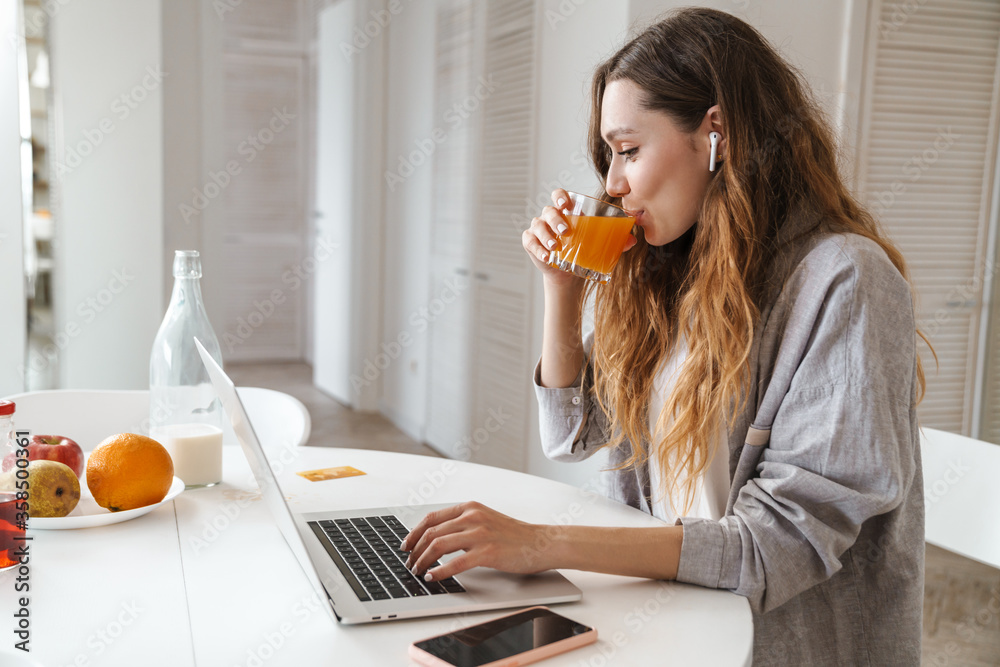 Poster Portrait of pleased woman drinking juice while working with laptop