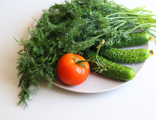 fresh cucumbers, tomato and dill in a white plate on a white background
