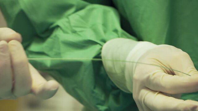 Doctor putting small wire in thin plastic tube in medical clinic, catheter