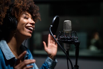 An young professional smiling energetic african female singer wearing headphones is performing a...