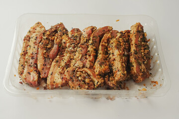Fresh pork belly slices in Korean style marinate and herbs on a plastic tray on simple table cloth.