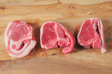 Three raw fresh lamb loin chops on a wood cutting board. Top view. Meat industry and food preparation concept.