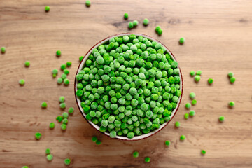 Frozen green peas in a bowl with few scattered on the wooden table