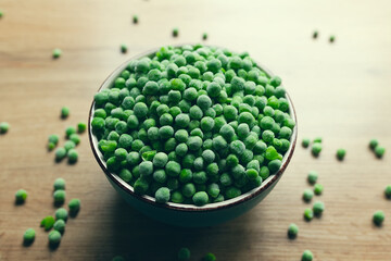 Frozen green peas in a bowl with few scattered on the wooden table