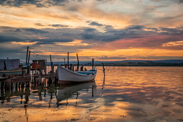 Fototapeta premium amazing colorful sunset at a lake with a boat at a wooden pier. Horizontal view