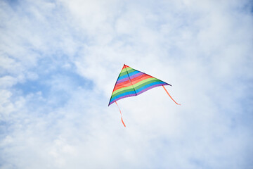 Colorful vivid rainbow kite flying on light blue cloudy sky in summer. Family leisure activity. Happy springtime lifestyle. Child toys. Sky landscape background.