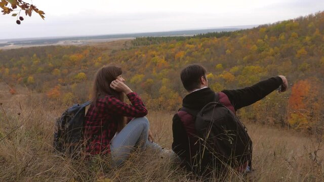 travelers take pictures on smartphone against backdrop of beautiful autumn landscape. Free travelers man and woman with backpacks take selfie on break in fall. teamwork travelers. travel concept