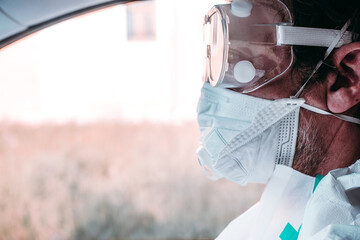 Fototapeta na wymiar Man wearing protective COVID costume, mask, respirator and gloves. Doctor closeup stay and looking forward on pink and white wall background. Pandemic, self-isolation and quarantine finish concept.