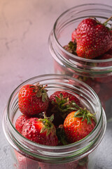 Fresh ripe strawberry fruits in two glass jars, summer vitamin berries on grey stone background, angle view