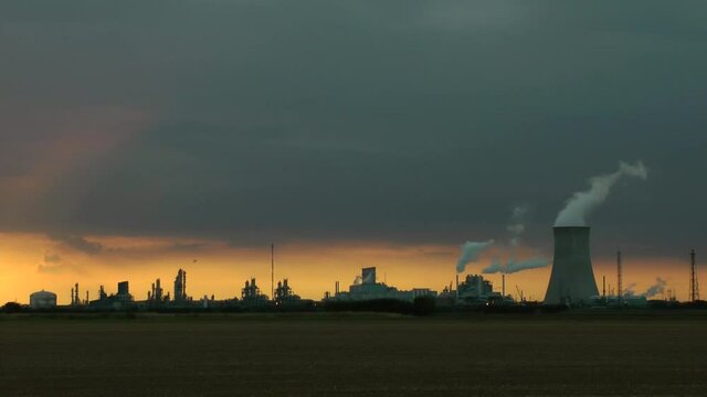 Cooling towers at oil refinery with steam. Sun setting sky. Time lapse