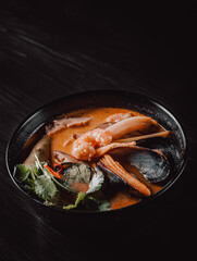 pan asian food. Tom Yum soup in black bowl on black wooden table background