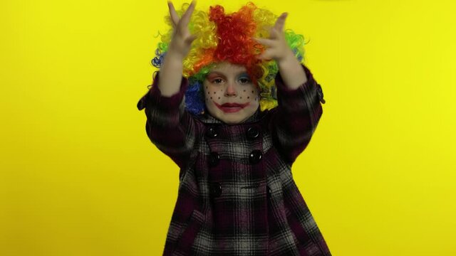 Little child girl clown in colorful wig making silly faces. Having fun, shows tricks. Halloween