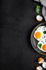 Fried eggs on frying pan on black desk top-down copy space