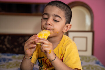 Happy little boy eating mango (lockdown activities)