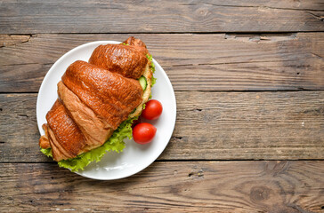 Croissant sandwich with chicken breast and lettuce. Croissant sandwich on a wooden table. Delicious nutritious breakfast. Free space for text.