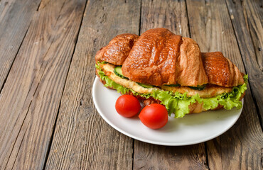 Croissant sandwich with chicken breast and lettuce. Croissant sandwich on a wooden table. Delicious nutritious breakfast. Free space for text.