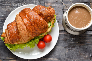 Croissant sandwich with chicken breast and lettuce. Croissant sandwich and coffee on a wooden table. Delicious nutritious breakfast. Free space for text.