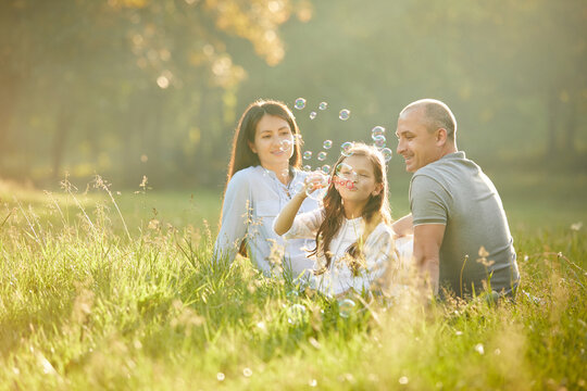 Happy Family With Child Girl Blow Soap Bubbles Outdoor In Sunny Summer Day