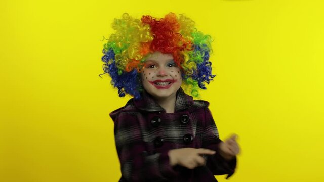 Little child girl clown in rainbow wig making silly faces. Having fun, smiling, dancing. Halloween