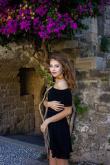 Greece, Rhodes - 07/11/2018: A beautiful girl in a black dress stands near a tree with flowers. Girl in the spring.