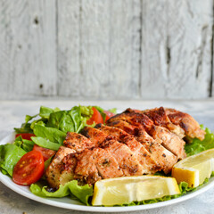Grilled chicken breast salad with spinach and tomatoes. Healthy eating Fried chicken breast, lemon, cherry tomatoes, spinach and lettuce. Light background.