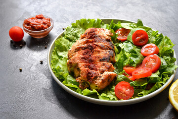 Grilled chicken breast salad with spinach and tomatoes. Healthy eating Fried chicken breast, lemon, cherry tomatoes, spinach and lettuce. Dark background.