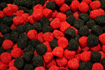 A pile of berry marmalades in shape of raspberries red and black color in sugar dusting. Colourful candy background


