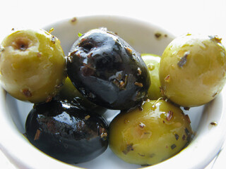 Close-up of green olives and black olives in marinade and spices in a white bowl