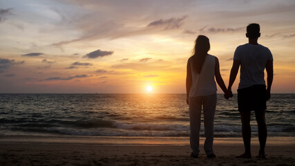 silhouette of young people walking on beach to boundless ocean water joining hands at orange sunset backside view