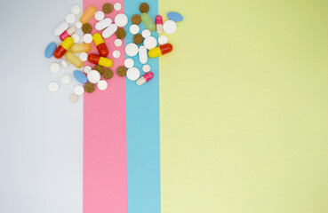 A lot of colorful tablets and pills on a striped background of white, blue, pink and yellow with a copy space