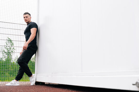 A pensive Caucasian fitness trainer in full growth stands on light background. Conceptual photo on the sports ground, online training