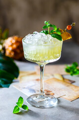 Cold freshly squeezed pineapple juice with crushed ice and mint on a light gray concrete background.