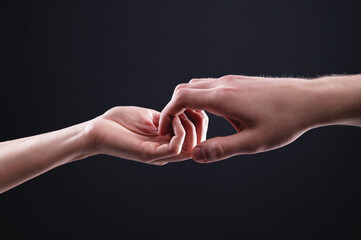 Two hands male and female ordinately hold each other symbolizing the help and mutual support between men and women on a black background studio shooting
