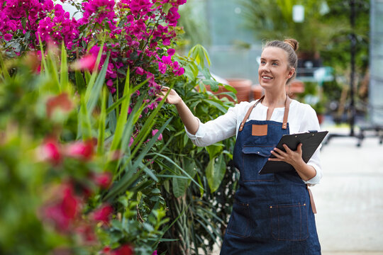 Female small business owner holding clipboard. Portrait of a young woman at work in greenhouse in uniform and clipboard in her hand . Greenhouse produce.