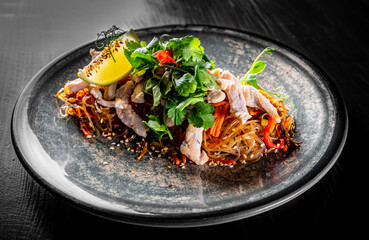 Udon stir-fry noodles with chicken meat, vegetables and sesame in plate on black wooden table background