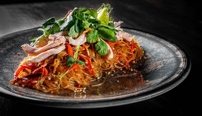 Udon stir-fry noodles with chicken meat, vegetables and sesame in plate on black wooden table background