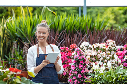 Flowers and technology. Attractive young woman holding a digital tablet in a garden center. Quality control in the greenhouse. Young woman holding digital tablet checking the growth in a greenhouse
