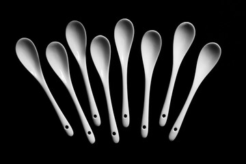 .eight white porcelain spoons lies on a black background isolated macro close shot from above