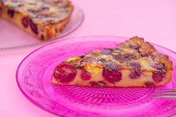 Slice of english cherry cake on a pink plate, with cake in background, wood table