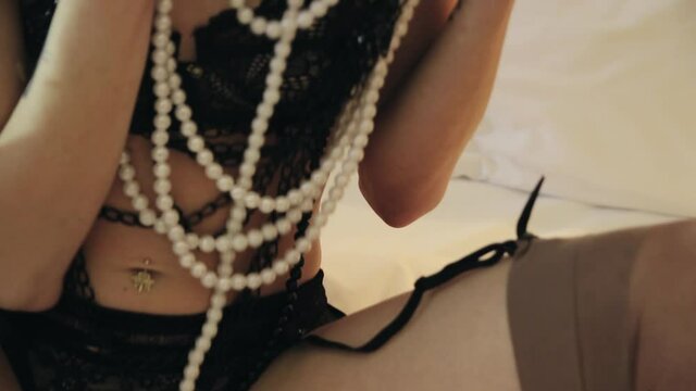 Slender girl with black lace underwear and with black and white pearl beads on the chest and waist