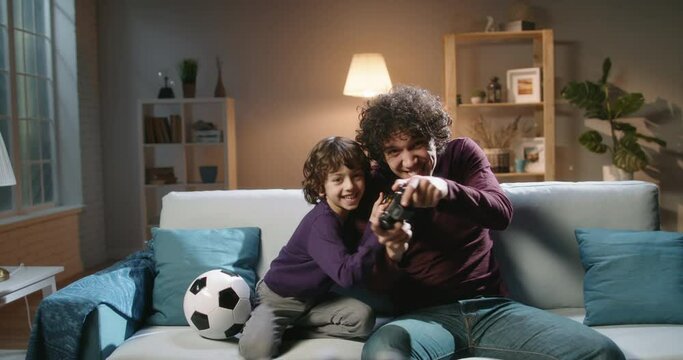 Cute authentic asian brothers with curled hair enjoying their together time, playing football video games in front of tv, parent and son relaxing with their hobby 4k footage