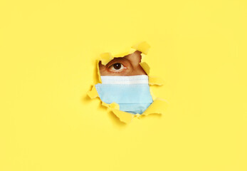 A woman with a medical face mask looks through a hole in yellow paper wall