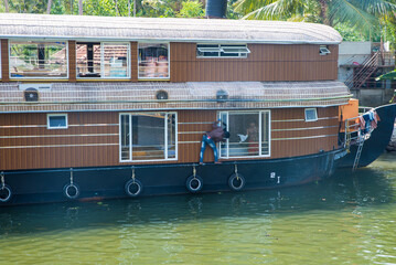 Fototapeta na wymiar Small houses in a local village located next to Kerala's backwater on a bright sunny day and traditional Houseboat seen sailing through the picturesque backwaters of Allapuzza or Alleppey in Kerala 