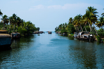 Obraz premium Small houses in a local village located next to Kerala's backwater on a bright sunny day and traditional Houseboat seen sailing through the picturesque backwaters of Allapuzza or Alleppey in Kerala 