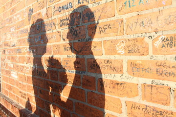 Shadows of lovers on an old brick wall with names on it